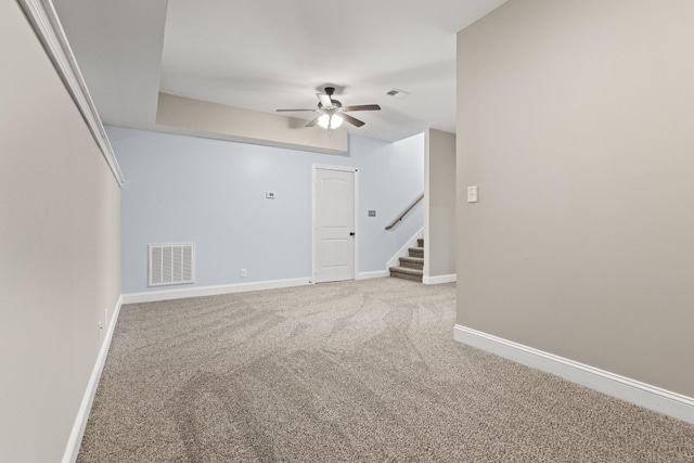 carpeted empty room featuring stairs, a ceiling fan, visible vents, and baseboards