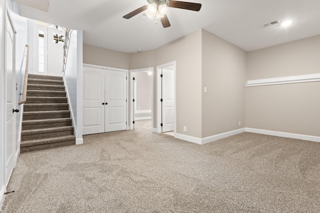 carpeted empty room with visible vents, baseboards, a ceiling fan, and stairway