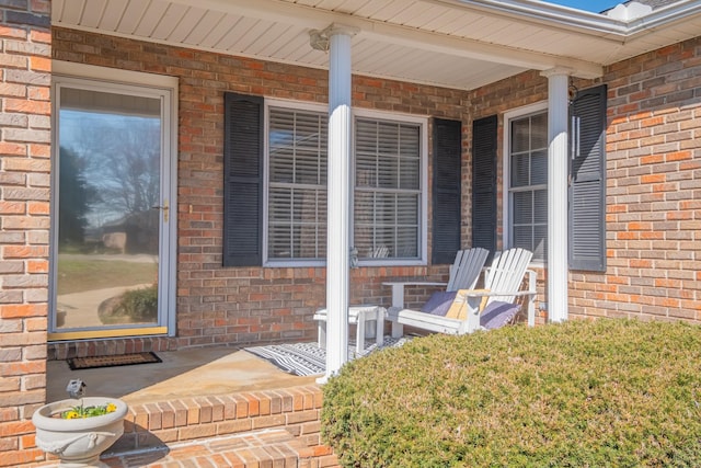 view of exterior entry with brick siding and covered porch