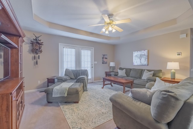 living room featuring light colored carpet, baseboards, a tray ceiling, and a ceiling fan