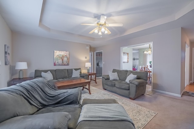 carpeted living room with baseboards, a raised ceiling, and ceiling fan with notable chandelier