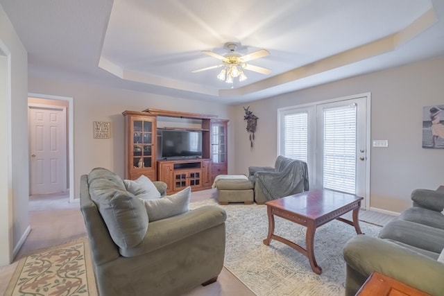 living area with a raised ceiling, baseboards, and ceiling fan