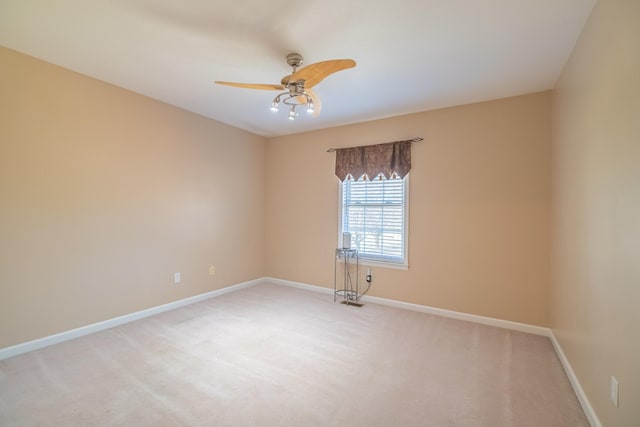 spare room featuring a ceiling fan, light colored carpet, and baseboards