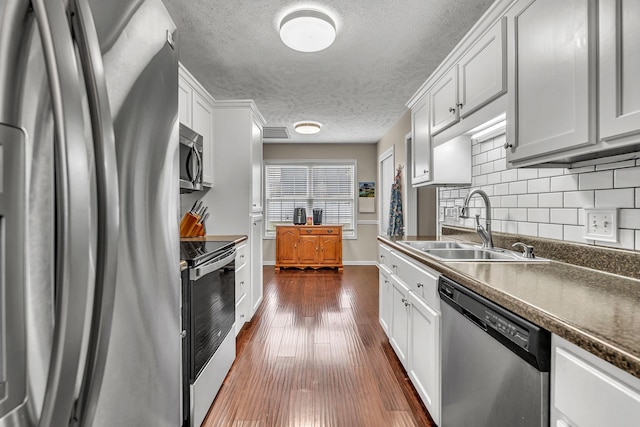 kitchen with dark wood-style flooring, a sink, appliances with stainless steel finishes, dark countertops, and tasteful backsplash