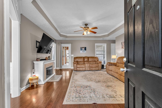 living area with a glass covered fireplace, crown molding, a tray ceiling, and wood finished floors