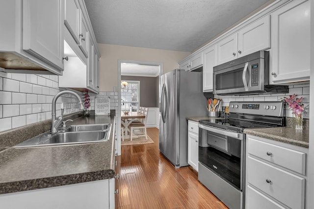 kitchen with dark countertops, a wainscoted wall, appliances with stainless steel finishes, and a sink