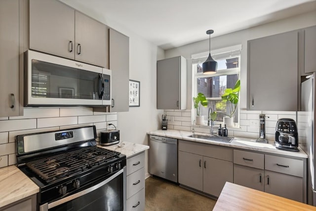 kitchen featuring gray cabinetry, a sink, decorative light fixtures, tasteful backsplash, and stainless steel appliances