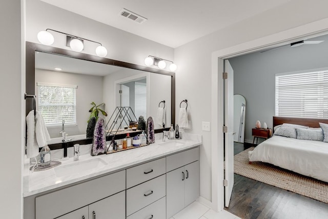 ensuite bathroom with a sink, visible vents, wood finished floors, and double vanity