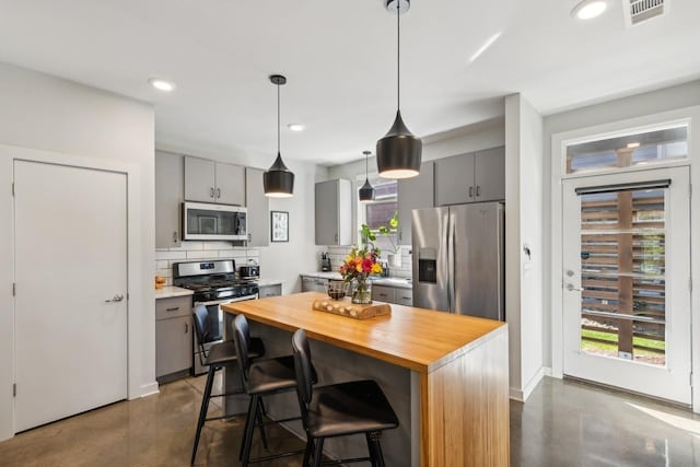 kitchen with finished concrete floors, gray cabinetry, stainless steel appliances, wood counters, and tasteful backsplash