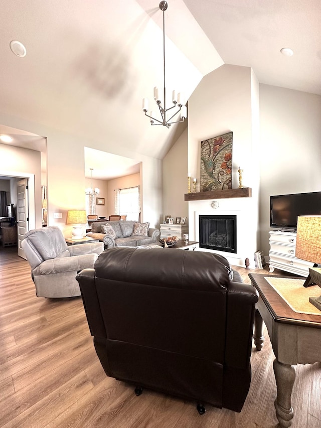 living room featuring a notable chandelier, high vaulted ceiling, a glass covered fireplace, and wood finished floors