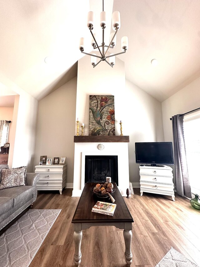 living room with a notable chandelier, a fireplace, wood finished floors, and vaulted ceiling