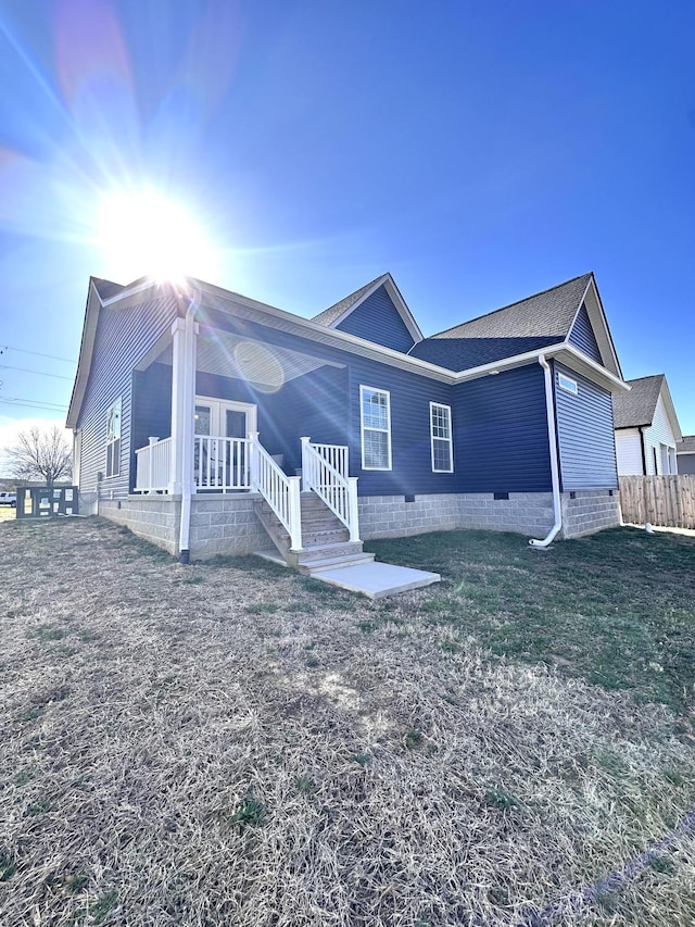 rear view of property featuring crawl space, covered porch, a shingled roof, and fence