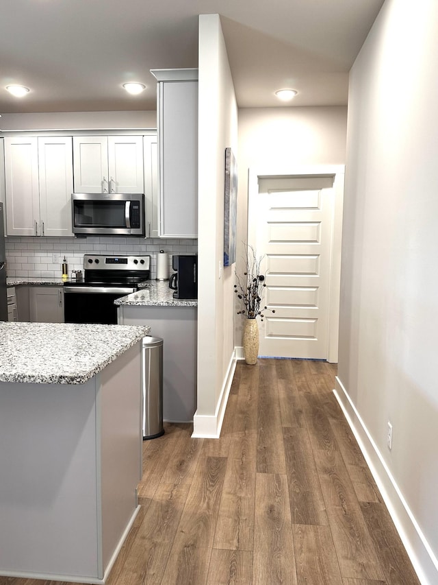 kitchen with decorative backsplash, light stone counters, wood finished floors, and appliances with stainless steel finishes