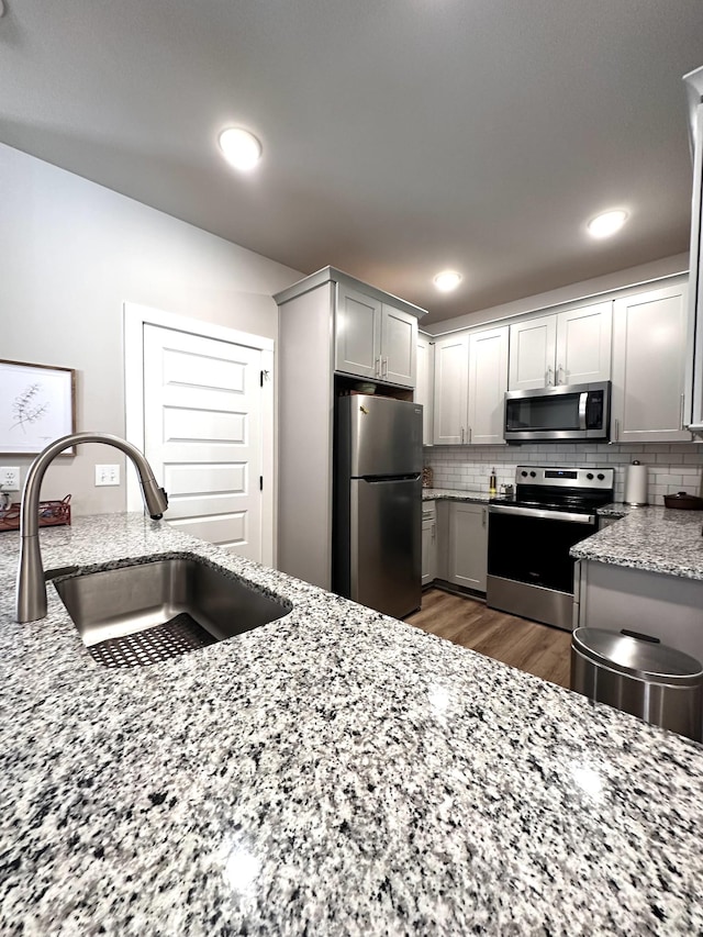 kitchen with light stone counters, dark wood finished floors, a sink, stainless steel appliances, and tasteful backsplash