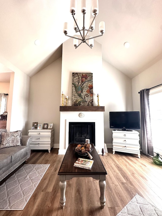 living area featuring lofted ceiling, wood finished floors, a fireplace, and a chandelier