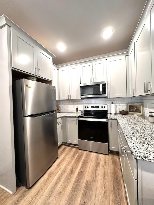 kitchen with light stone countertops, light wood finished floors, gray cabinetry, appliances with stainless steel finishes, and backsplash