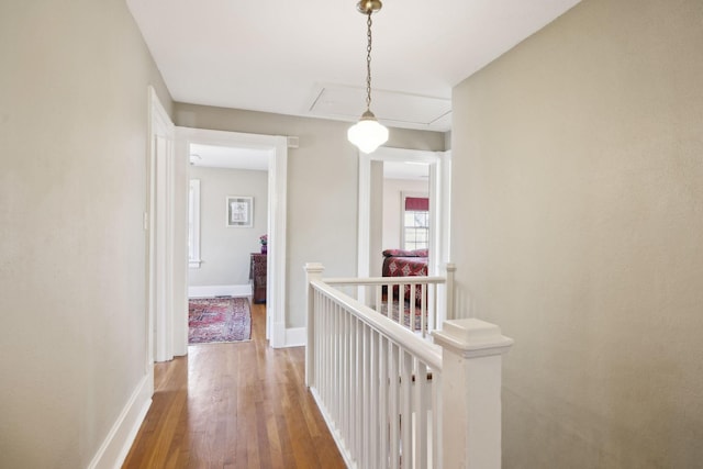 hall featuring wood finished floors, attic access, an upstairs landing, and baseboards