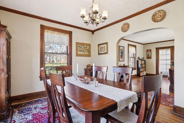 dining area featuring crown molding, baseboards, wood finished floors, arched walkways, and a notable chandelier