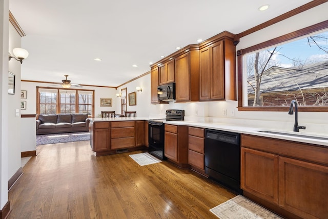 kitchen featuring dark wood finished floors, a peninsula, a sink, black appliances, and light countertops