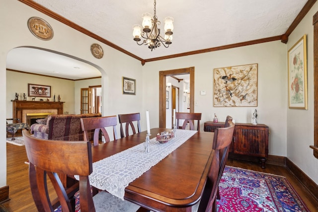 dining room with ornamental molding, wood finished floors, arched walkways, a fireplace, and baseboards