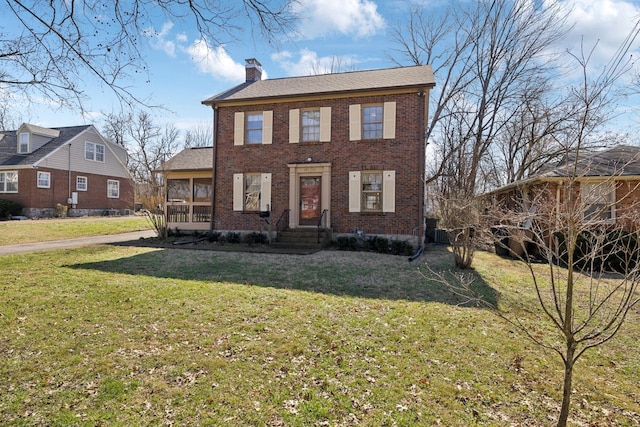 colonial home with brick siding, a front yard, and a chimney