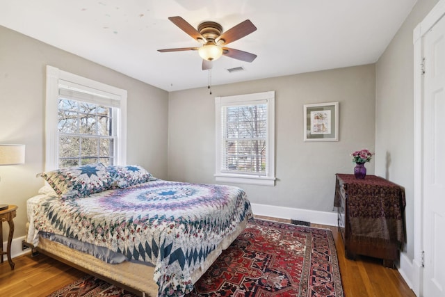 bedroom featuring visible vents, multiple windows, wood finished floors, and baseboards