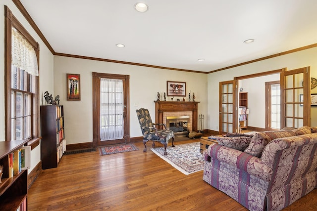 living area featuring wood finished floors, baseboards, ornamental molding, french doors, and a glass covered fireplace