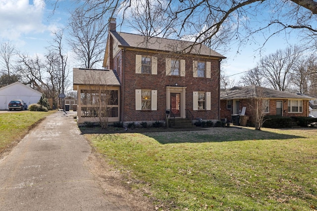 colonial inspired home featuring a front yard, brick siding, driveway, and a chimney