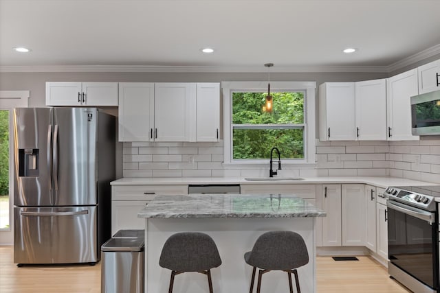 kitchen featuring crown molding, a breakfast bar area, appliances with stainless steel finishes, white cabinetry, and a sink