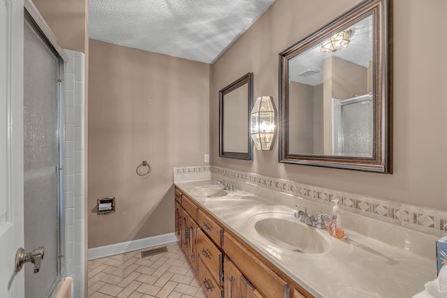 bathroom with an enclosed shower, a textured ceiling, baseboards, and a sink