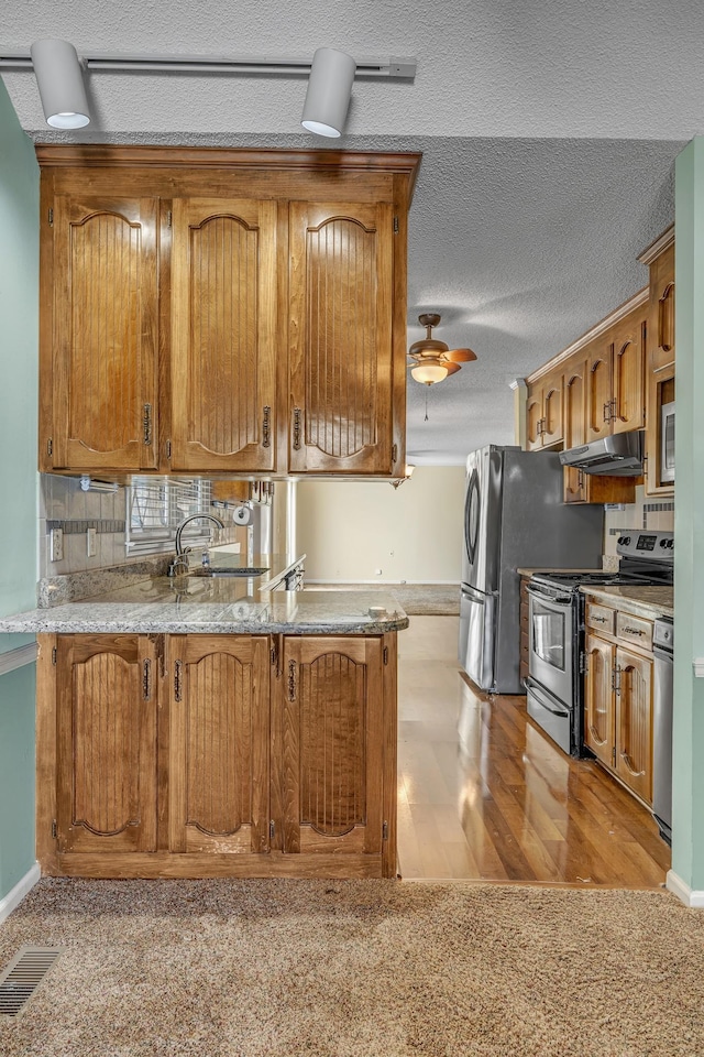 kitchen with visible vents, under cabinet range hood, stainless steel appliances, brown cabinetry, and ceiling fan