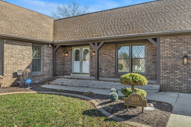 entrance to property with brick siding, french doors, and roof with shingles