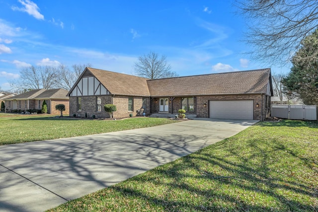 tudor house featuring fence, concrete driveway, a front yard, roof with shingles, and an attached garage