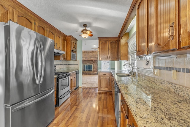 kitchen with brown cabinets, a sink, under cabinet range hood, wood finished floors, and appliances with stainless steel finishes