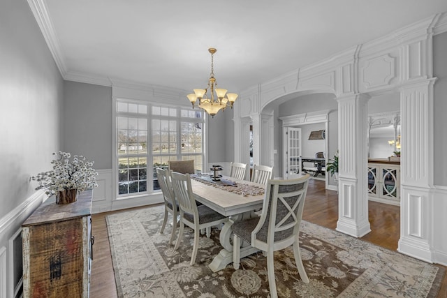 dining room with a decorative wall, arched walkways, wood finished floors, and ornate columns