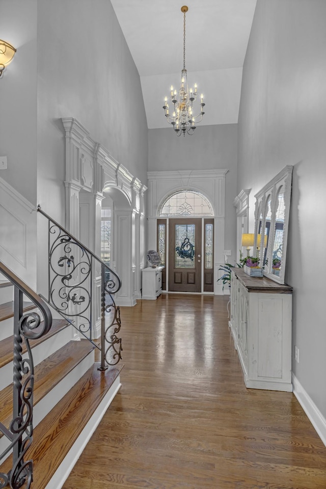 foyer with high vaulted ceiling, an inviting chandelier, wood finished floors, and stairs