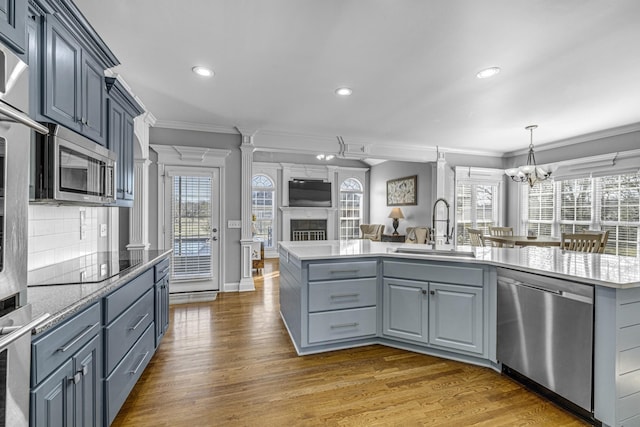 kitchen featuring crown molding, open floor plan, wood finished floors, stainless steel appliances, and a sink