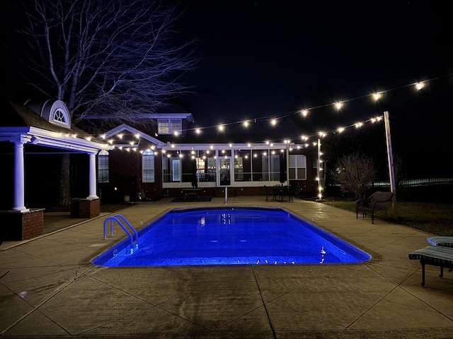 pool at night featuring a patio and an outdoor pool