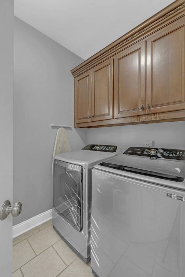 clothes washing area with washing machine and dryer, light tile patterned floors, cabinet space, and baseboards