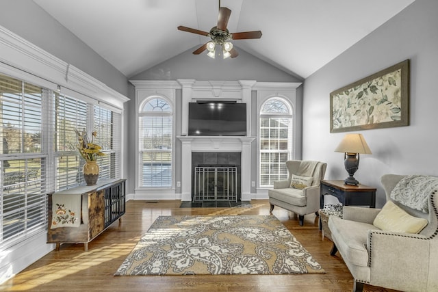 living room featuring ceiling fan, baseboards, a tiled fireplace, lofted ceiling, and wood finished floors