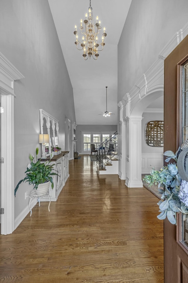 entryway with stairway, ceiling fan with notable chandelier, a towering ceiling, wood finished floors, and ornate columns