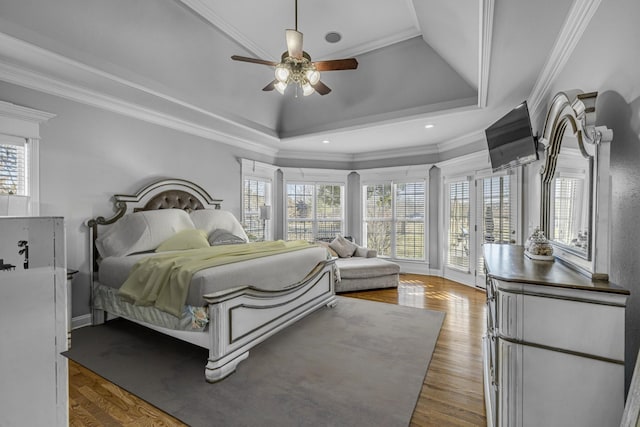 bedroom with a raised ceiling, wood finished floors, and crown molding