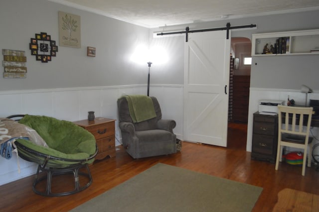 living area with a barn door, ornamental molding, wood finished floors, and wainscoting