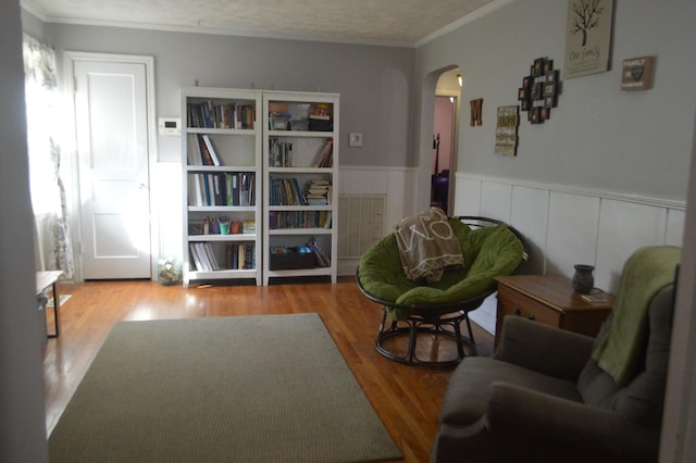 living area featuring arched walkways, visible vents, wood finished floors, and a wainscoted wall