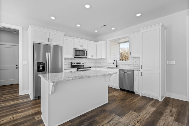 kitchen featuring a kitchen island, appliances with stainless steel finishes, dark wood-style floors, white cabinets, and a sink