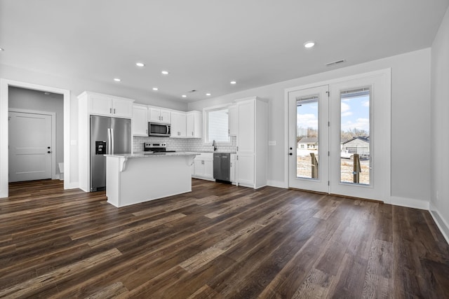 kitchen with a center island, decorative backsplash, white cabinets, stainless steel appliances, and dark wood-style flooring