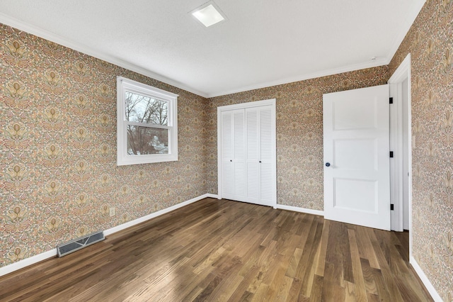 unfurnished bedroom with visible vents, wood finished floors, a closet, wallpapered walls, and baseboards