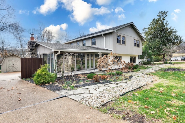 view of front of house with a shingled roof, an outdoor structure, a chimney, and a sunroom