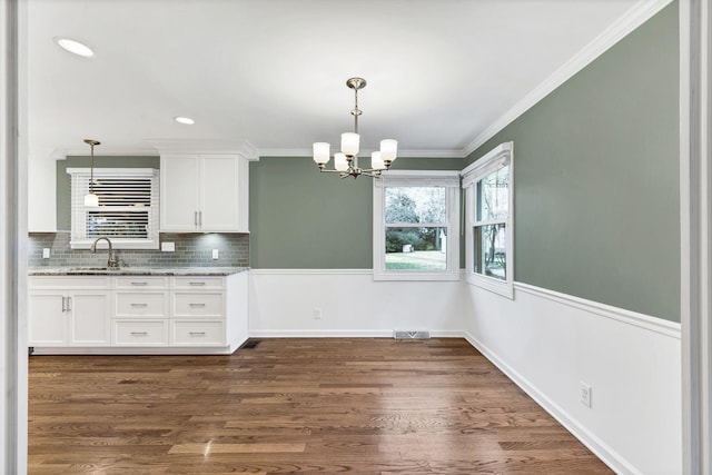 unfurnished dining area with baseboards, dark wood-style flooring, a sink, ornamental molding, and a notable chandelier