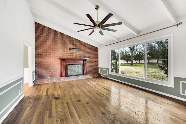 unfurnished living room featuring a brick fireplace, brick wall, ceiling fan, lofted ceiling with beams, and wood-type flooring